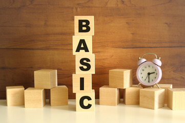 Five wooden cubes stacked vertically on a brown background make up the word BASIC.