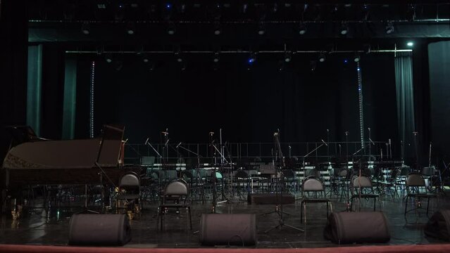 A cinematic shot of a scene without people in the Philharmonic hall before a musical concert with dramatic lighting. Lots of empty chairs and microphones for musicians.