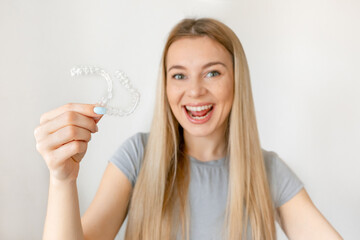 Happy girl holds a whitening mouth guard for teeth. The girl aligns her teeth with the help of...