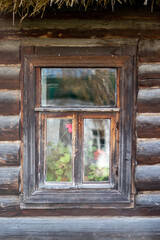 Window in an old log house. View of a fragment of the wall of a house made of old cylindrical logs. Reflection in a lonely window of a wooden house.