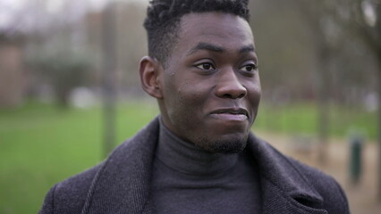 Satisfied young black African man walking outside at park nature feeling happy