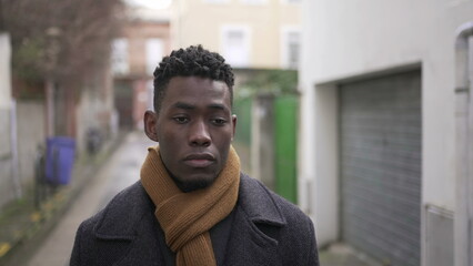 Sad upset black African man walking outside in city with moody depressed emotion