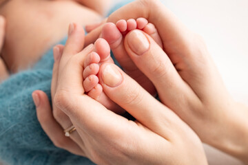 Fototapeta na wymiar Mother is doing massage on her baby foot. Close up baby feet in mother hands on a blue background. Prevention of flat feet, development, muscle tone, dysplasia. Family, love, care, and health concept