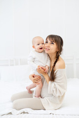 happy mom with a baby daughter at home on the bed hugs and kisses, happy young mother and motherhood