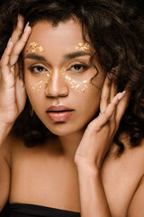 curly african american woman with golden paint on face looking at camera isolated on black.