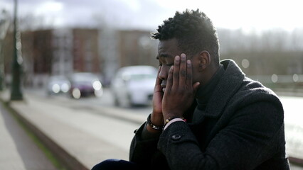 Preoccupied black African man sitting at city street curb feeling anxiety