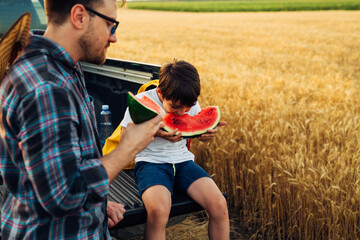 Son and father eat watermelon in the field