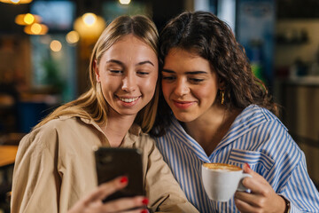 Front view of two women looking at phone in a cafe