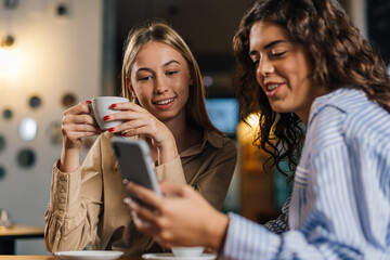 Two women look at the phone while drinking coffee