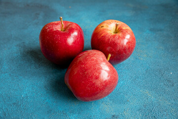 Three red apples lie on a blue background
