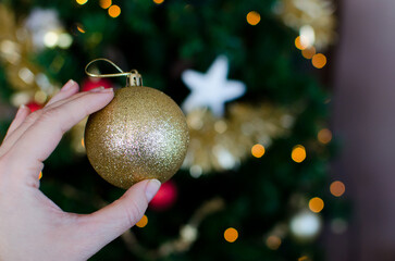 Mano humana sujetando una bola de purpurina dorada con el árbol de navidad de fondo