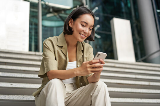 Technology And Communication. Young Smiling Girl, Asian Woman Sits With Smartphone, Reads Message With Big Smile