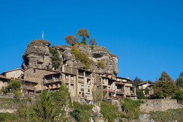 Set of houses and stone buildings in the highest part of the town of Rupit. Above the houses the top of a steep stone hill with few trees and an independent Catalan flag
