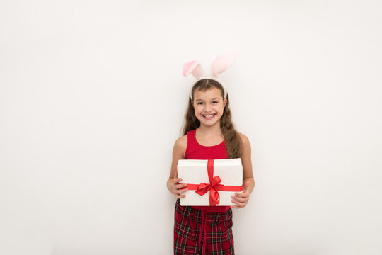  little girl holding gift box on gray background, A beautiful girl with rabbit ears stands and dreams. Christmas gifts concept.