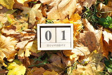 Wooden calendar block with date on falling autumn leaves background.