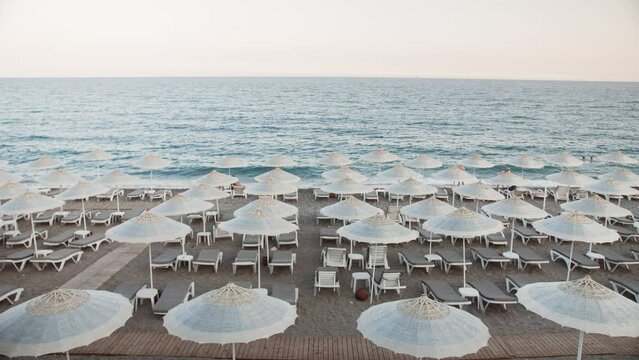 Empty Beach, Rows of folded beach umbrellas and empty sunbeds in Turkey, early morning. Italy or Greece. Top view. Travel and leisure concepts.