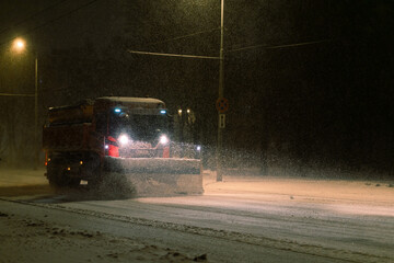 A snow plow cleans city streets at night in a blizzard