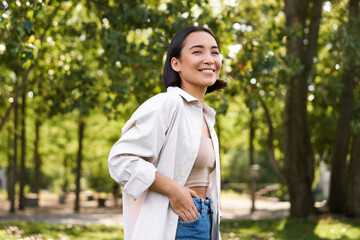 Modern people. Happy young asian girl walking in park, smiling and enjoying beautiful summer day