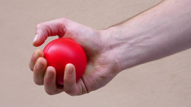 A man hand shows red stress ball and starts squeezing and releasing it