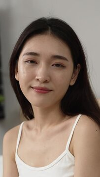 Vertical Screen: portrait with closeup shot of an beautiful asian female wearing white strap tank is turning to look at the camera with a smile in a bright bed chamber at home