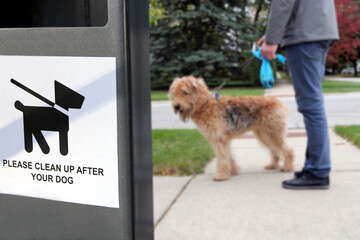 The warning sign: Clean up after your dog. Man is walking with his dog outside.