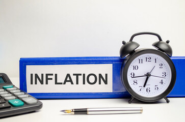 The word Inflation is written on a notepad and a white background with a pen and a folder for documents