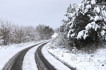 Obraz premium Scenic view of empty, not cleared road with snowy landscape during snowfall in winter season. Right turn onto a slippery winter road. A gloomy winter day. Ukraine.