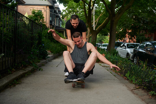 Male pushing same sex partner on skateboard.