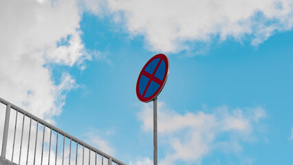 A round road sign signifying a ban on stopping vehicles against a background of blue sky and white clouds. Tools regulating the rules of the road.