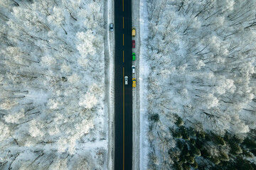 Aerial view of winter landscape with snow covered woods and black asphalt forest road on cold wintry day