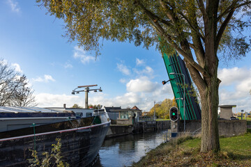 Empty inland vessel sails through an open bridge into a lock with a green light