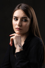 Portrait of a young brunette with long hair in the studio. Dramatic photo in dark colors. A girl with a snake tattoo on her arm.