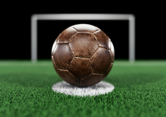 Worn and scratched brown leather football on penalty spot, with goal post and net in background....