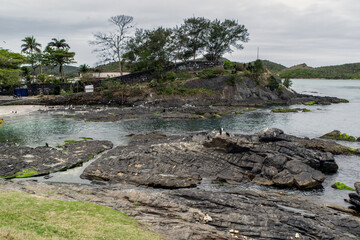 As linda praia do forte em volta do Forte São Mateus em Cabo Frio, com muitas Rochas, a água do mar correndo entre elas e montanhas em volta.