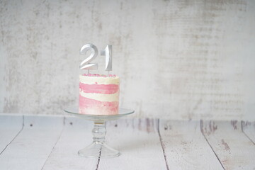 21st Birthday cake pink and silver cake with some sprinkles and 21st candlelight on a white wooden background.                       