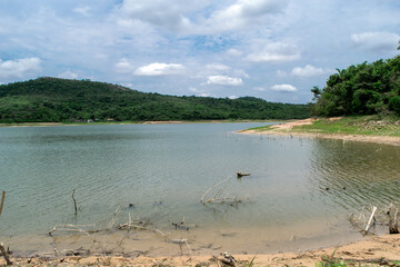 Linda vista da lagoa Várzea das Flores em contagem, com as águas banhando a orla, céu nublado e montanha ao fundo.