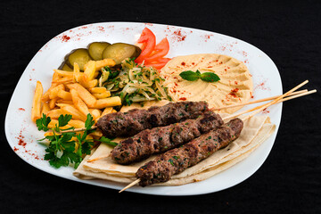 Dinner kebab, barbecued beef on a stick with tomatoes, french fries, hummus, pickles, tortilla and...