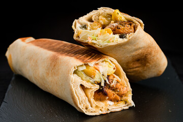 Shawarma from chicken, tomatoes, sweet pepper, herbs, sauce and pita bread on a dark background.