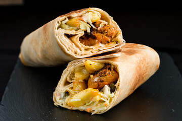 Fresh shawarma from chicken, tomatoes, sweet pepper, herbs, sauce and pita bread on a dark background.