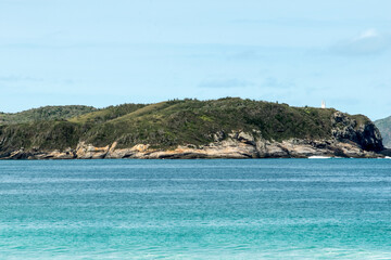 Orla do Chateau Recanto das Dunas na Praia das Dunas, com ondas fortes, lindo c&eacute;u azul e farol encima de rochedo.