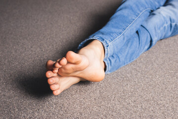 Bare feet of a girl in jeans sitting on the floor. Foot and leg