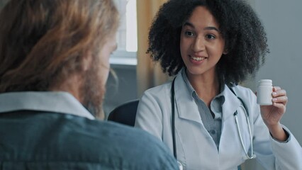 African doctor therapist ethnic woman pharmacist help sick male patient give bottle with tablets drug treatment cardiac pills female physician medic recommend antibiotic dosage pharmaceutic medicine