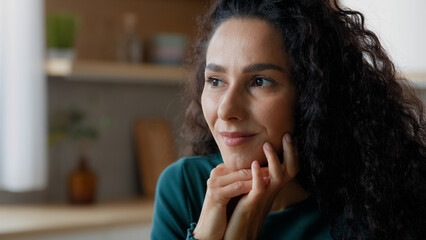 Close up head shot portrait peaceful beautiful young woman relaxing at home put chin on folded palms looking into distance spanish curly lady remembering positive moments dreaming about carefree life 