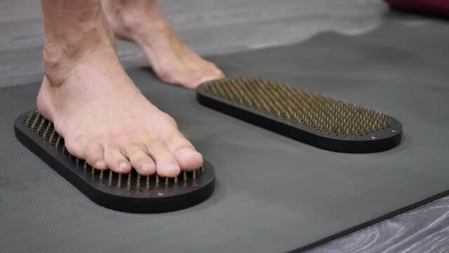 A man with bare feet steps on Sadhu's boards with sharp nails to gain energy and release stress. Nail standing exercises. Indian practice board Rishi.