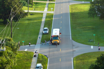 Top view of standard american yellow school bus picking up kids at rural town street stop for their...