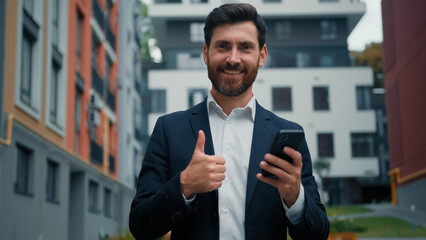 Successful businessman caucasian bearded man employee manager use internet city wifi chatting messages online point finger on modern phone making thumb up approval gesture enjoy cell mobile connection