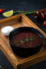 Russian borscht soup made from beets, potatoes, cabbage, onions and spices with sour cream and bread on a wooden board.