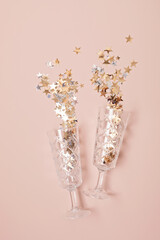 Champagne or sparkling wine glasses with confetti over pink background. Christmas, new year party, birthday or wedding celebration idea. Top view, flat lay, copy space