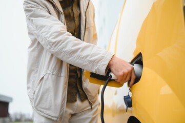 Man Holding Power Charging Cable For Electric Car In Outdoor Car Park. And he s going to connect the car to the charging station in the parking lot near the shopping center