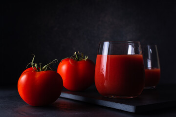 tomato juice in a transparent glass with fresh tomatoes on a black surface against the background of a soft backdrop close-up. dark artistic photo with copy space. selective focus